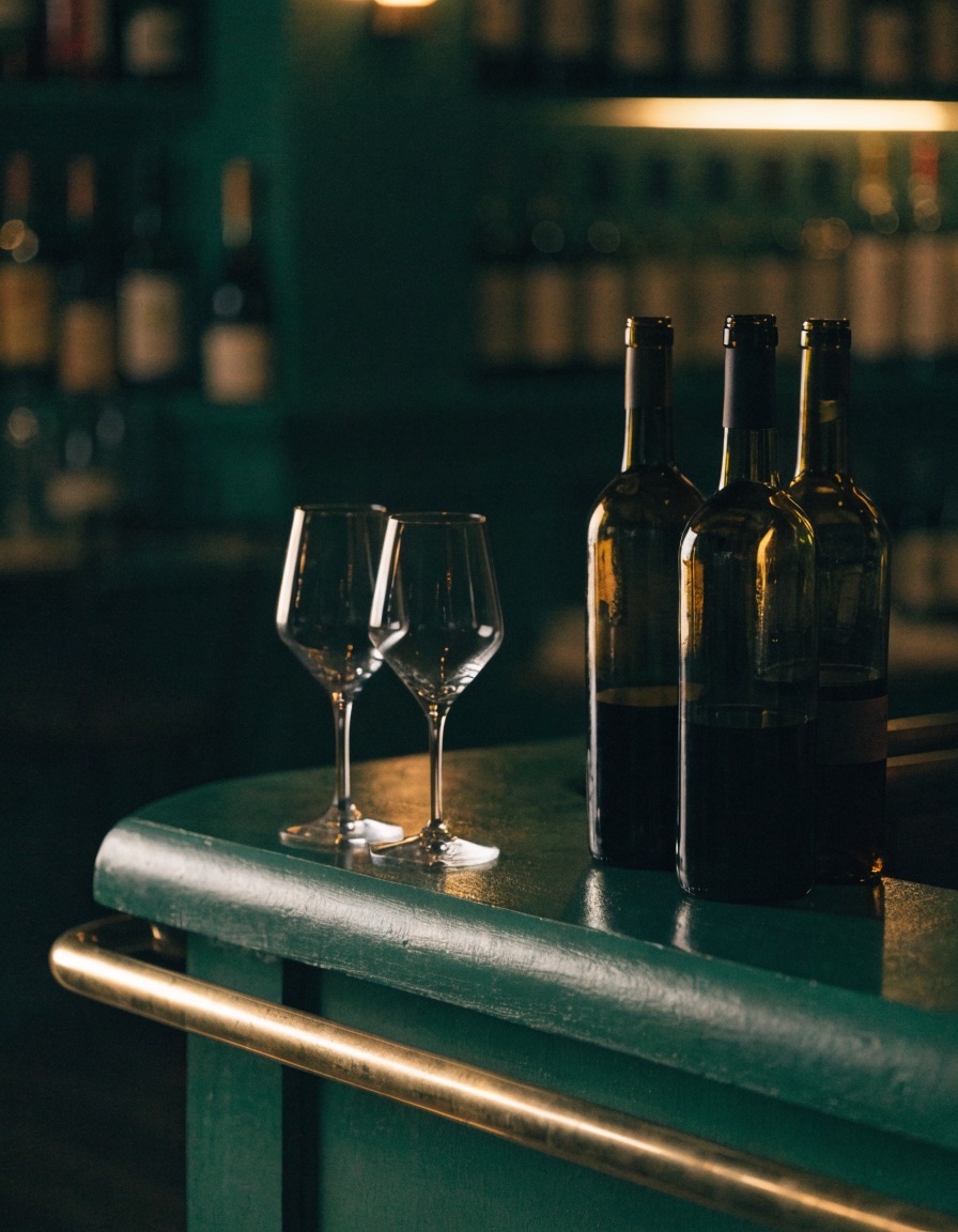 Weinbar mit dunkelgr&uuml;ner Front, Messingreling und offenen Flaschen